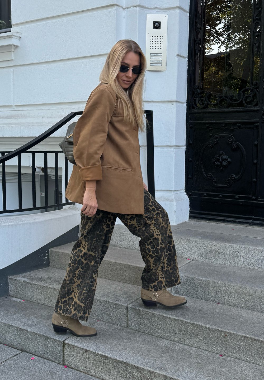 Καφέ σουέτ μπουφάν, παντελόνι με λεοπάρ σχέδιο και φαρδιά πόδια, ανοιχτό καφέ μπότες μέχρι τον αστράγαλο με διακοσμητικά στοιχεία και γυαλιά ηλίου, κατεβαίνοντας από πέτρινες σκάλες.