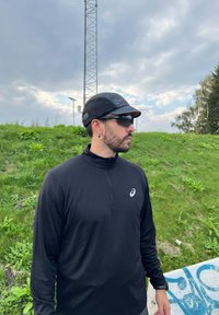 Melnas garās piedurknes sporta krekls ar rāvējslēdzēja apkakli, viegls, valkāts kopā ar melnu sietu cepuri un tumšām saulesbrillēm. Teicama auskaru detaļa.