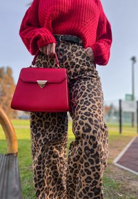 Pulover roșu tricotat cu mâneci largi, pantaloni cu imprimeu leopard și talie înaltă, și o geantă roșie cu accesorii aurii și un detaliu triangular.