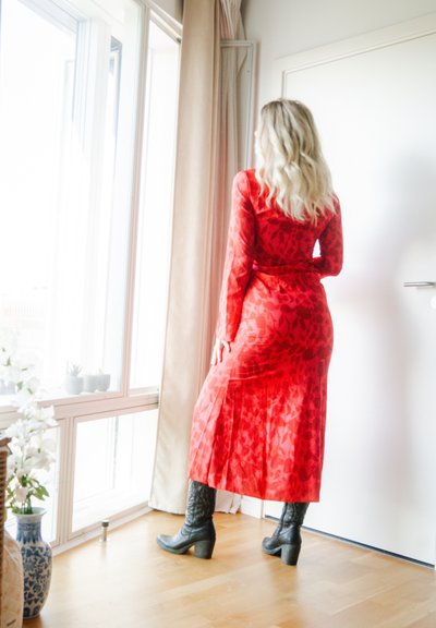 Vestido largo de patrón floral rojo con mangas largas, tejido semitransparente, cintura ajustada y falda acampanada, combinado con botines negros hasta el tobillo.