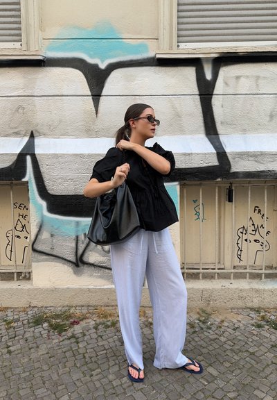 Top peplum negro con mangas cortas, pantalones de pierna ancha a rayas azul claro, y un bolso negro estilo slouchy. El fondo presenta graffiti.