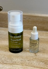 Elemis Superfood Hautpflegeprodukte auf beigem Stein: 30 ml Gesichtsspray mit Pumpzerstäuber und kleine klare Flasche mit Pipette.
