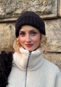 Berretto a coste nero in maglia e giacca bianca con zip in ecopelliccia, caratterizzata da un collo alto e dettagli a contrasto neri e strutturati.