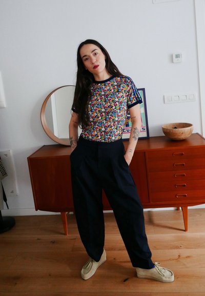 Top de manga corta con estampado floral y detalles en azul marino, metido en pantalones de talle alto y pierna ancha también en azul marino, combinado con zapatos beige. Interior minimalista.
