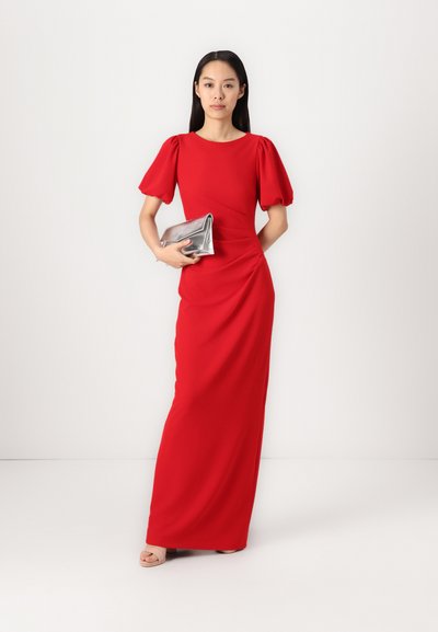Vestido maxi rojo ajustado con mangas abullonadas, diseño drapeado y textura suave; combinado con un clutch metálico plateado y tacones nude.