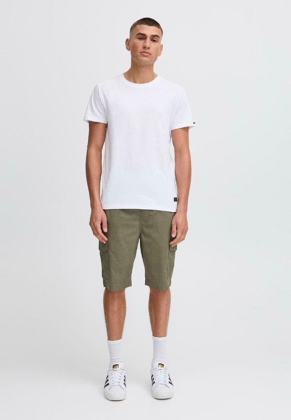 T-shirt bianco in cotone abbinato a pantaloni cargo verde oliva con tasche laterali, completato da sneakers bianche e calzini alla caviglia.