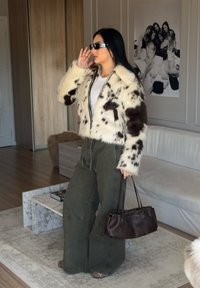 Faux fur-jacka med vita och bruna fläckar, svart dragkedja, kombinerad med olivgröna vida byxor och en liten brun handväska. Svarta solglas�ögon på.