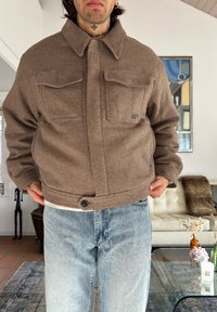Veste marron en mélange de laine avec un col en suède et deux poches avant, fermeture par boutons à la taille, portée avec un jean bleu clair.