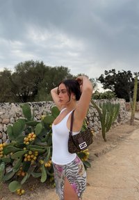 Borsa a tracolla marrone a fantasia con forma rettangolare, abbinata a un top bianco aderente e una gonna colorata e fantasiosa con spacco laterale.