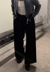 Fekete, széles szárú nadrág, texturált anyagból, hozzá illő, testhez simuló fehér atléttel és szürke cipzáras dzsekivel. Vastag talpú fekete cipő viselve.