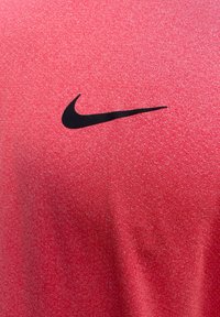 Piros sportpóló strukturált anyagból, elülső részén kiemelkedő fekete Nike logóval.