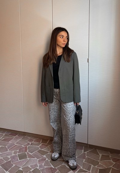 Blazer gris sobre una blusa negra, combinado con pantalones de leopardo de corte amplio. Los accesorios incluyen un bolso negro pequeño y zapatillas blancas.