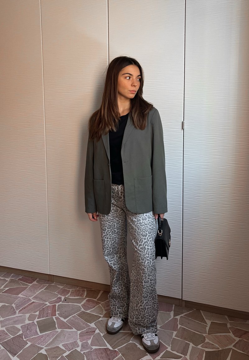 Sakou gri peste un top negru, asortat cu pantaloni evazați cu imprimeu leopard. Accesoriile includ o mică geantă neagră și adidași albi.