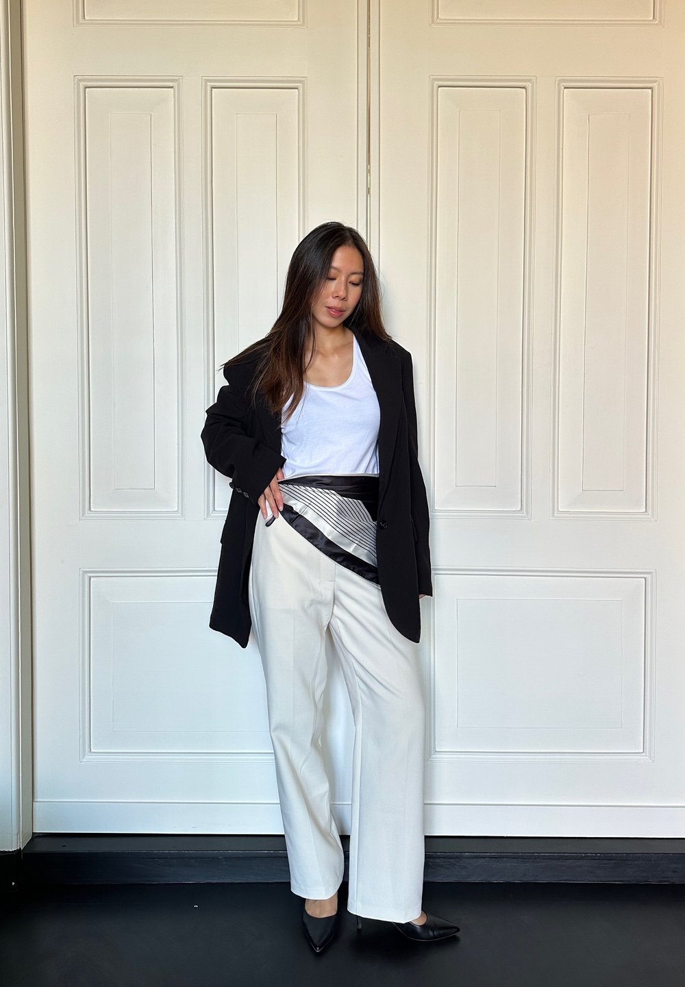 Sort blazer over en hvid tanktop, parret med brede beige bukser. Har et bælte med sort og sølv-mønster og sorte spidse hæle.