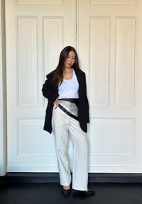 Sort blazer over en hvid tanktop, parret med brede beige bukser. Har et bælte med sort og sølv-mønster og sorte spidse hæle.