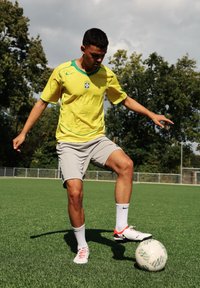 Sárga Nike mez zöld kiegészítőkkel, szürke nadrággal és fehér zoknival. Egy zöld mintázatú focilabda műfüvön.