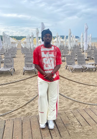 Camiseta gráfica roja con estampado blanco, combinada con pantalones blancos con rayas rojas. Sillas de arena y tumbonas en un entorno de playa.