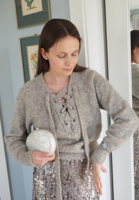 Grått strikket genser med snøring i halsen; holder en rund, hvit clutchveske. Paljettkjole reflekterer lys og tilfører glans til helhetsinntrykket.