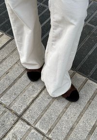 Pantaloni bianchi di corduroy con una superficie texturizzata, abbinati a scarpe nere e marroni con punta arrotondata e dettaglio a fiocco.