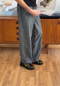 Black t-shirt, grey loose-fitting trousers with pockets, and black shoes featuring yellow accents. Standing on wooden floor by a cabinet.