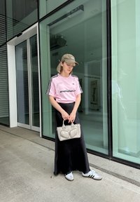 Lyserød t-shirt med korte ærmer, sorte striber og stjerner, sort maxi-nederdel, grå håndtaske og hvide sko med sorte striber.