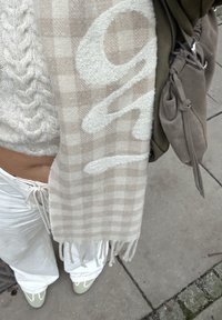 Vaaleanbeige ruudullinen huivi tupsureunuksin, yhdistettynä kermaiseen neulottuun villapaitaan ja väljiin valkoisiin housuihin. Pehmeä rakenne, ei näkyviä kuvioita.