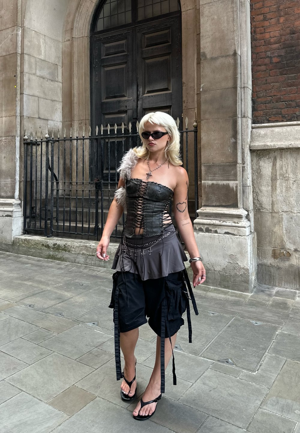 Must musta corset, millel on nööpidega esikülg, hall kihiline seelik, laiad mustad cargo-shortsid ja sussid. Aksessuaare moodustavad päikeseprillid ja kaelakee.