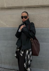 Sort læderjakke med høj krave, grå sweater under, brun lædertaske og en ternet skjorte bundet omkring taljen.