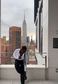 Zwarte broek en een wit, oversized overhemd met knoopjes, staand op een balkon met het Empire State Building op de achtergrond.