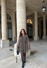 Φόρεμα με λεοπάρ σχέδιο, μακρυά μανίκια και σφιγμένο στη μέση. Συνδυασμένο με μαύρες ankle μπότες με τακούνι και μια μικρή μαύρη τσάντα. Ογκόλιθοι από πέτρα στο φόντο.