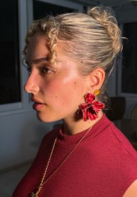 Guld runda örhängen med en röd blommönsterdesign, med lager av blad. Motivet bär en vinröd ribbad topp med hög hals.