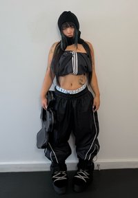Conjunto desportivo preto com um top curto riscado e calças largas. As botas são pretas com atacadores cinzas. Uma pequena bolsa preta é segurada com uma mão.