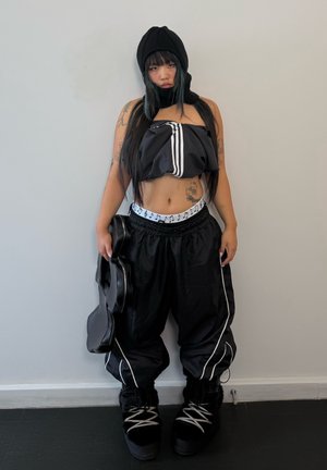 Svart sportig outfit med en kort topp med ränder och lösa byxor. Stövlarna är svarta med grå snörning. En liten svart väska hålls i ena handen.