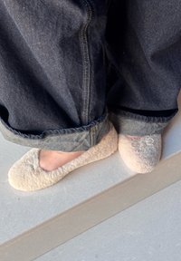 Chinelos felpudos de cor creme com uma textura suave e um pequeno laço decorativo em cima, combinados com jeans escuros, ligeiramente enfiados na bainha.