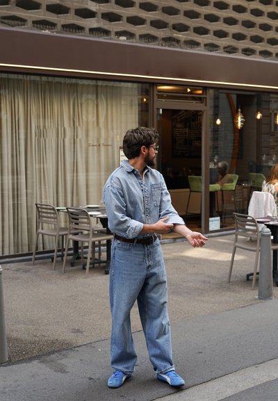 Conjunto de denim que incluye una camisa de botones azul clara y jeans de corte holgado, combinados con zapatillas azules. Un cinturón sencillo acentúa la cintura.