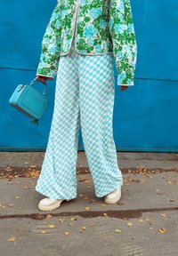 Vihreä kukkakuosisella vuorilla varustettu takki, siniset ruutukuosiset leveälahkeiset housut, valkoiset paksupohjaiset saappaat ja pieni sininen käsilaukku.