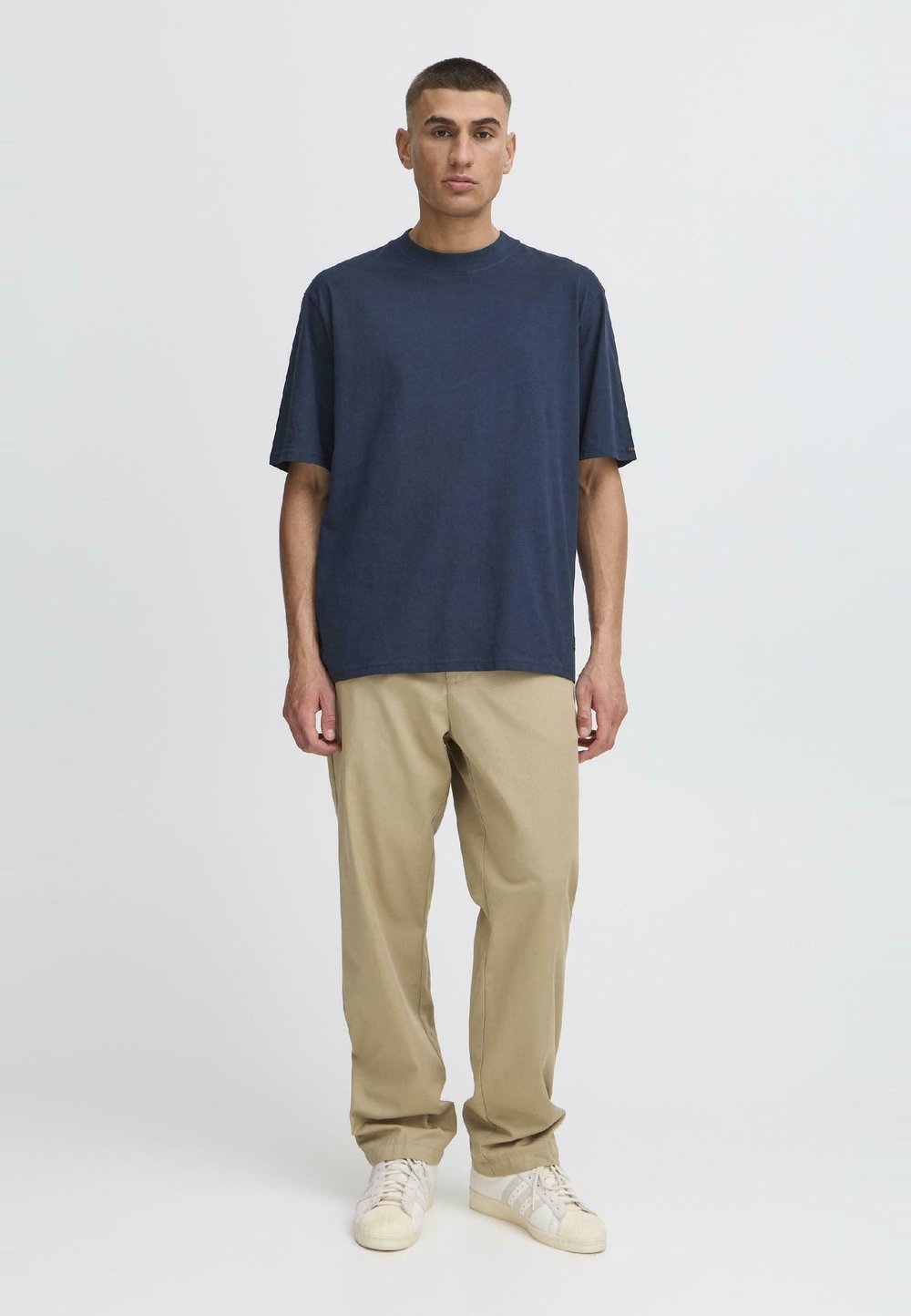 Navy bombažna majica s krojačkim ovratnikom, v kombinaciji s bež hlačami sproščenega kroja in belimi supergami z svetlimi poudarki. Preprost in modern dizajn.