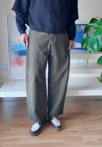 Široké nohavice olivovej zelenej farby s hladkou textúrou, doplnené o dvojfarebné topánky s bielym zvrškom a hnedou podrážkou.