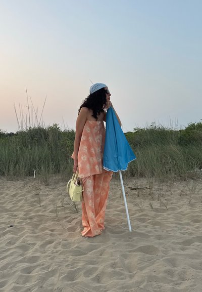 Conjunto de dos piezas con estampado floral de durazno, pantalones de pierna ancha, un sombrilla de playa ligera en azul y un pequeño bolso amarillo.