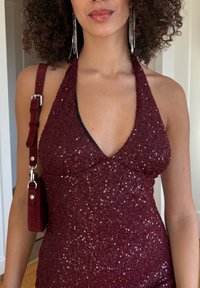 Bordó színű, pánt nélküli, flitterekkel díszített ruha, testhez simuló szabással. Hozzá illő, pántos táskával. Ezüstszínű fülbevalók.