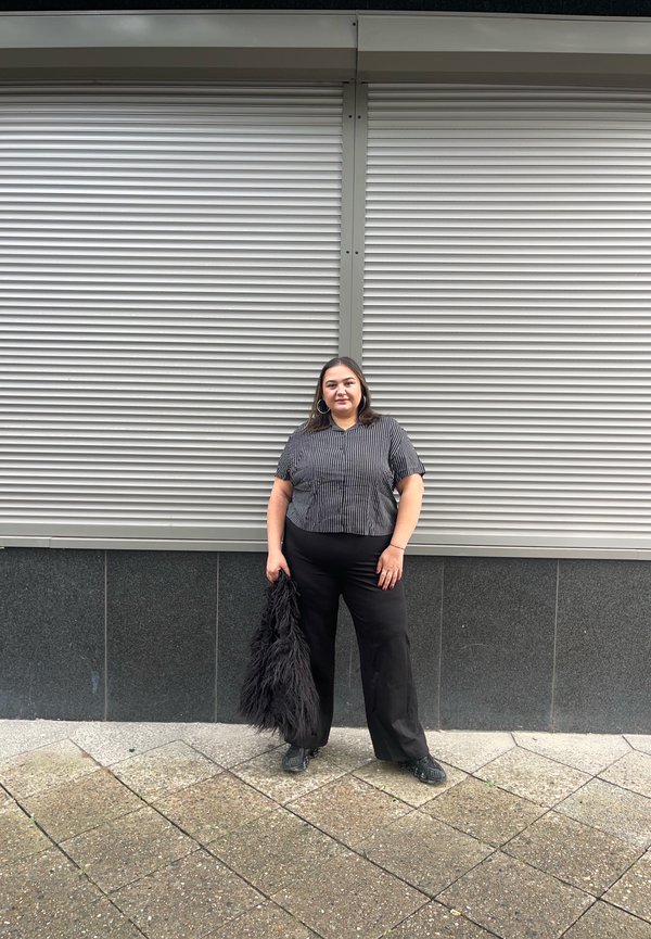 Black and white striped short-sleeved blouse with a round neckline, paired with wide black trousers and a fluffy black accessory. Flat shoes.