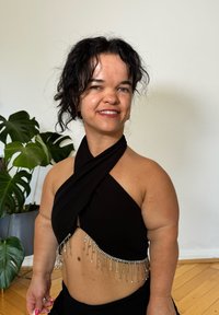 Haut à col halter noir avec un design drapé et des embellissements métalliques argentés le long de l'ourlet. Texture de tissu lisse, porté avec un bas noir.