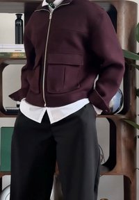 Veste bordeaux zippée avec deux poches frontales, tissu texturé, portée sur une chemise blanche, associée à un pantalon noir.