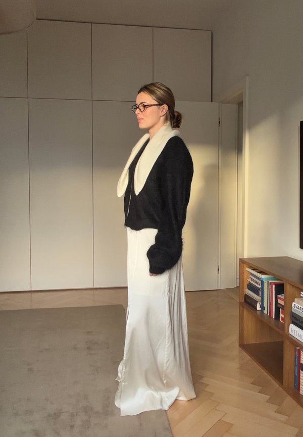 Sort kort sweater med hvid krave, båret over en lang cremefarvet satin nederdel. Glat tekstur og en sideslidsdetalje synlig.