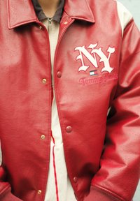Červená kožená bomber bunda se vyšívaným logem "NY" a "Tommy Jeans." S tlakové knoflíky a žebrovanými manžetami, s dvoutónovým designem.