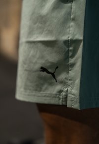 Αθλητικές σορτς σε ανοιχτό πράσινο χρώμα με μαύρο λογότυπο Puma στο στρίφωμα. Διαθέτουν ίσια γραμμή και ορατές ραφές.