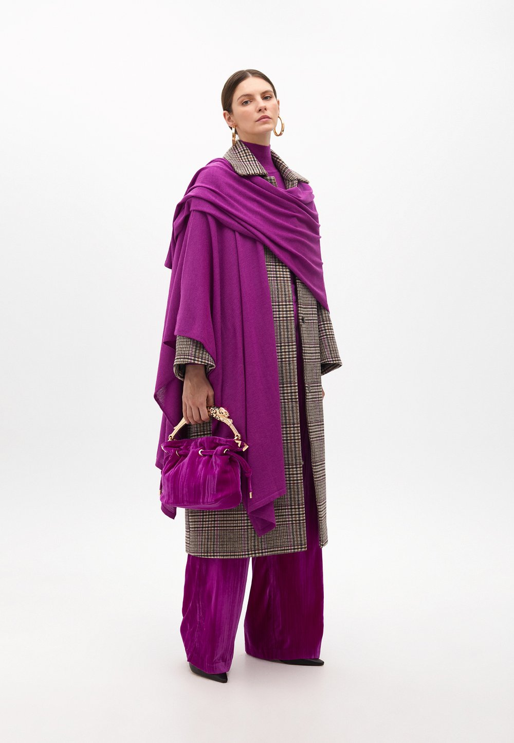 Fioletowy płaszcz, marynarka w kratę oraz �żywo fioletowe, plisowane spodnie. Trzyma małą, pluszową welurową torebkę z złotym uchwytem i ściągaczem.