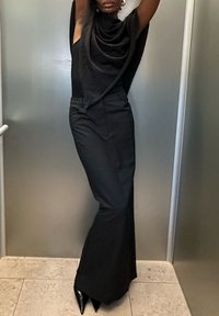 Čierny outfit pozostávajúci z drapovanej blúzky a priliehavých nohavíc, vyrobený z hladkej látky. Zameriava sa na lesklé ihličkové topánky a elegantný siluetu.