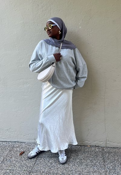 Sudadera de gran tamaño gris claro, falda maxi blanca brillante, pañuelo gris, gafas de sol grande y bolso blanco con detalles dorados.