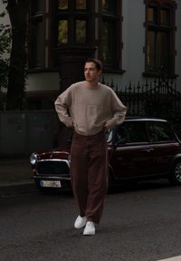 Beige strikket sweater, brede brune fløjlshorts og hvide sneakers. Model står på gaden med en vintage mørkerød bil i baggrunden.